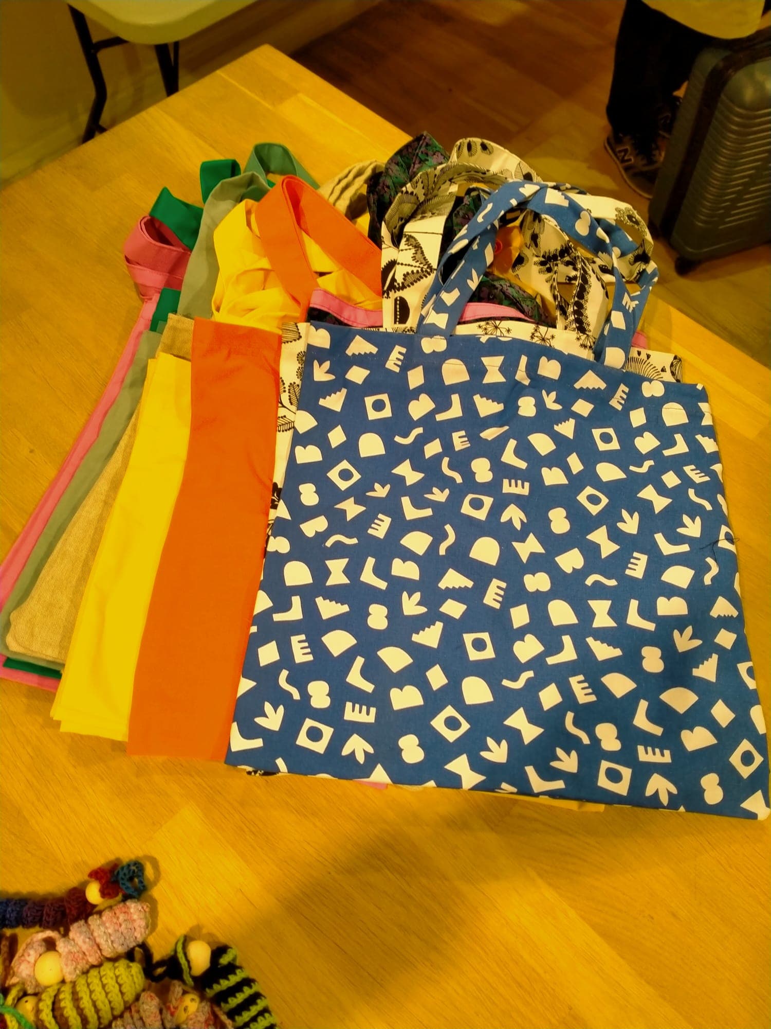 Pile de tote bags en tissu colorés, avec un modèle bleu à motifs géométriques blancs mis en avant